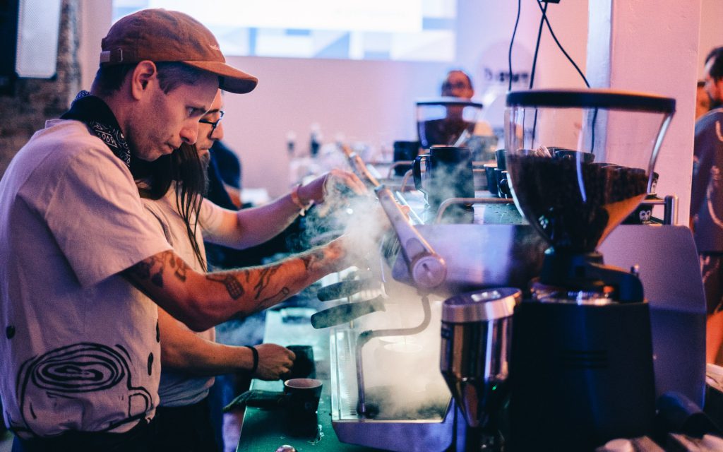 Baristas use an espresso machine to prepare drinks as part of a coffee competition