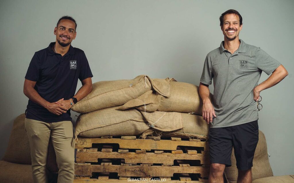 The owners of Baraka Coffee stand next  to bags of green coffee.