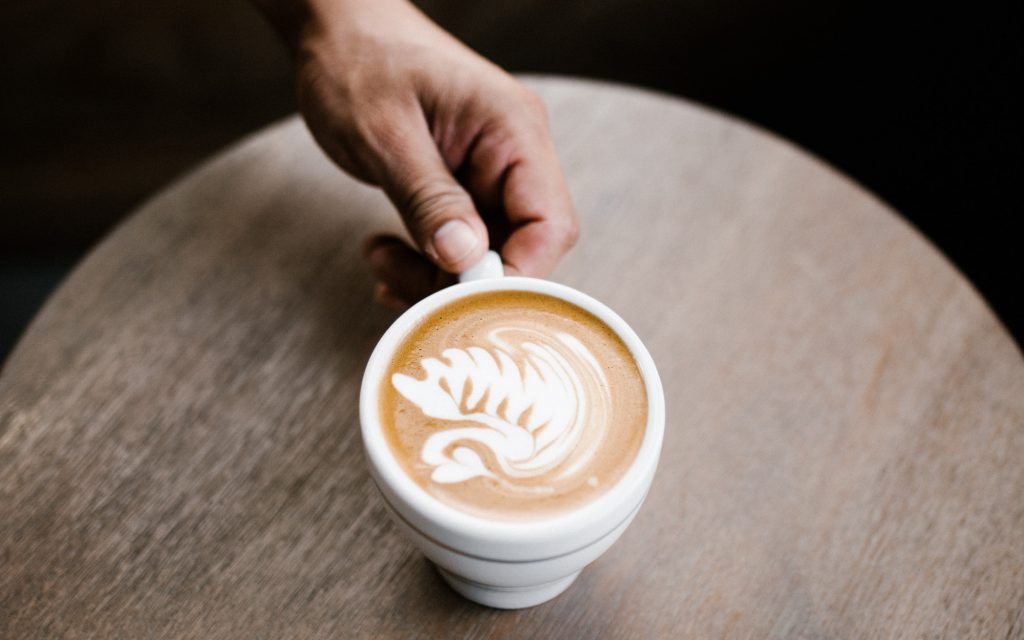 A coffee shop customer picks up a milk-based coffee drink with latte art.