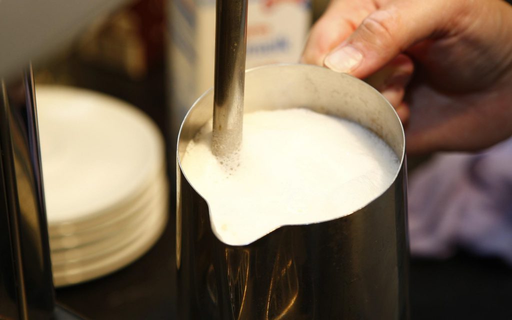 a barista steams milk in a jug